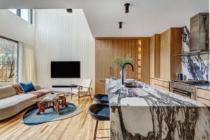 Open-concept living area with marble kitchen island, oak cabinets, and a wall-mounted TV on a white paneled wall