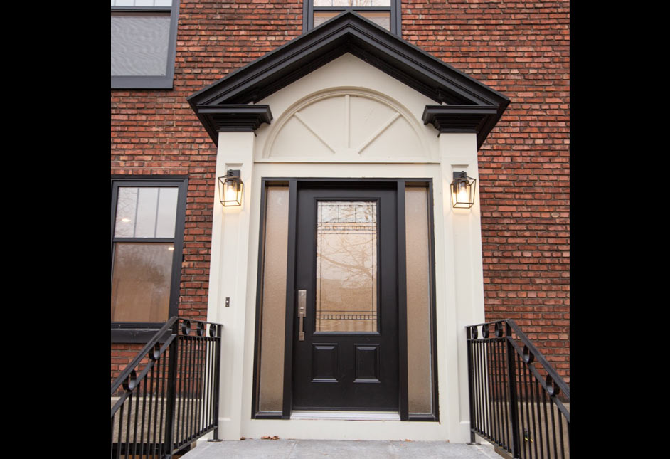 Black front door with sidelights and arched transom on a brick townhouse entrance, lit by two lanterns.