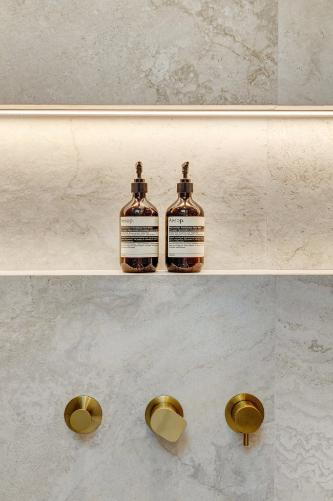 Two brown glass Aesop hand wash bottles with pump dispensers on a light marble shelf.