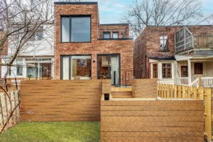 Brick building with large glass patio doors opening to a bright kitchen and living area, on a wooden deck.