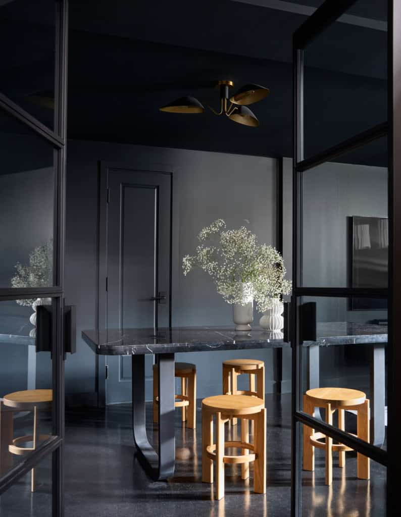 Dark, modern interior with black walls and marble countertop; white floral arrangement in a vase centered on the table, mirrored by glass panels.